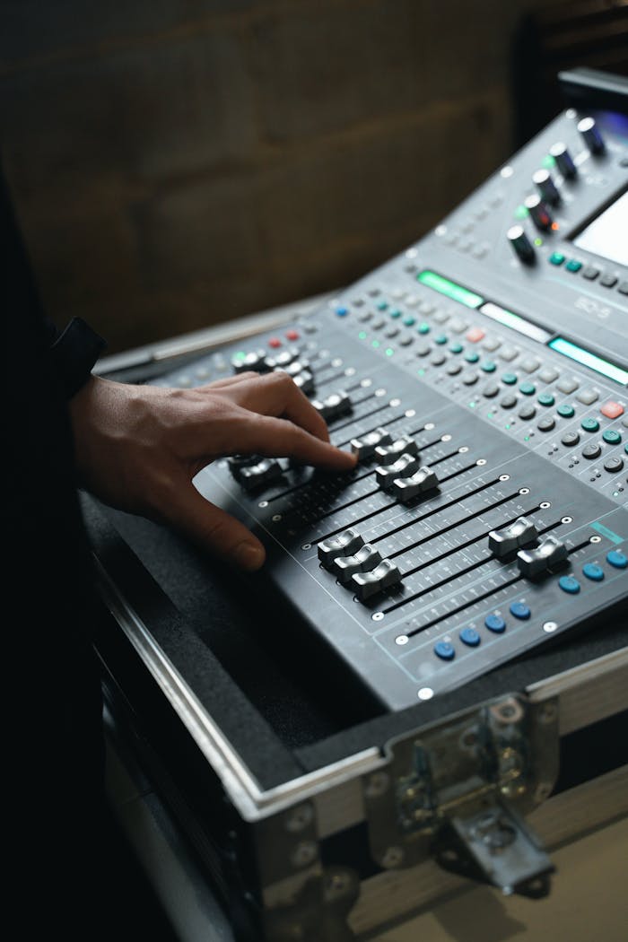 Close-up of a hand adjusting controls on a professional audio mixer in a studio setting.
