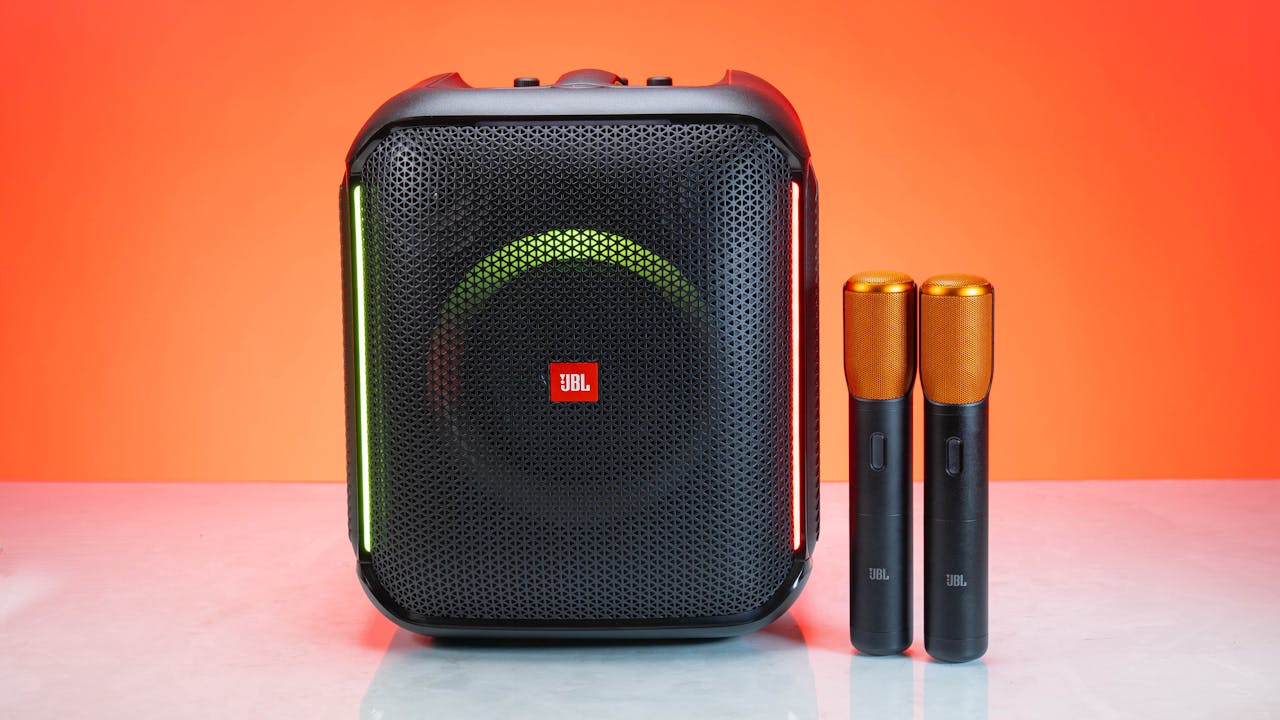 A wireless speaker with two microphones, set against a vivid orange background for a studio shoot.